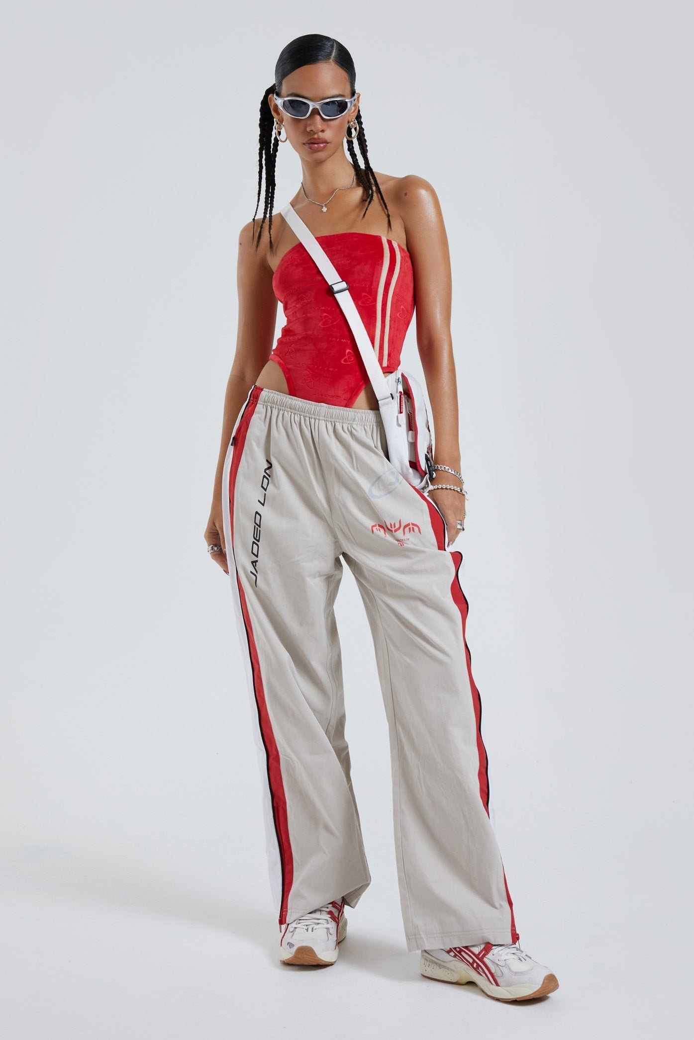 Female wearing red and almond oversized track pants with Jaded branding detail. Styled with a red bandeau bodysuit. 