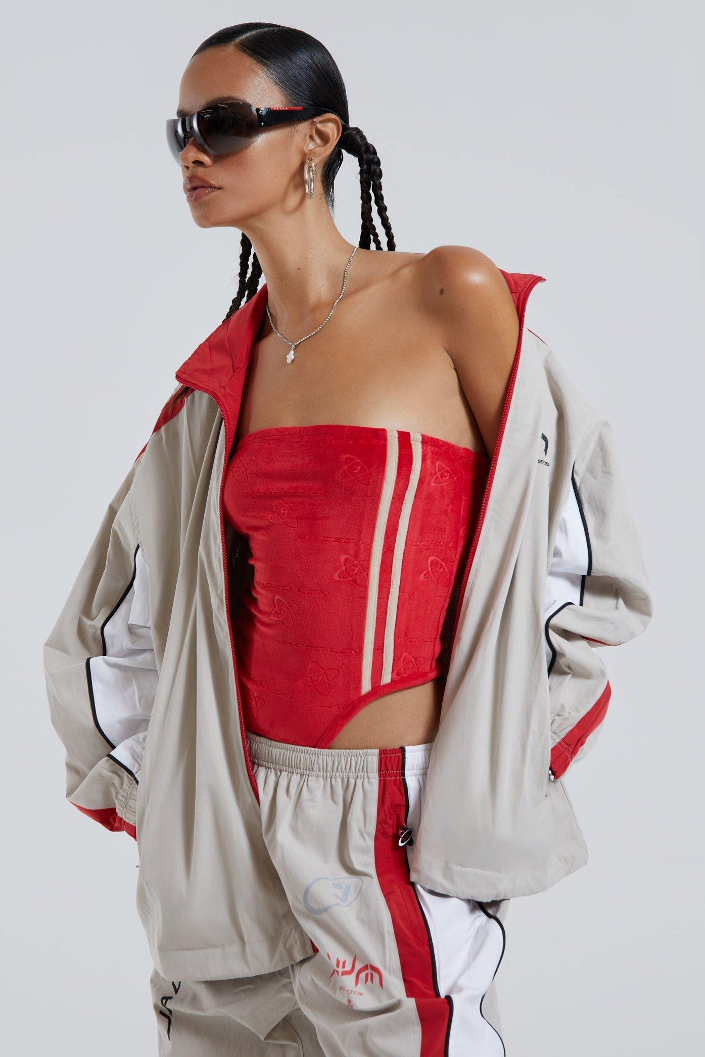 Female wearing red logo monogram embossed strapless bodysuit with stripe detail. Styled with almond track jacket and pants. 